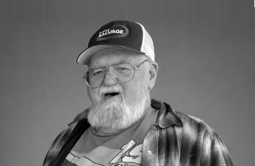 Elderly man wearing glasses and a Salvage branded cap, smiling against gray background