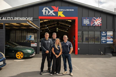 Four employees standing in front of Fix Auto Collision repair shop with red entrance and signage