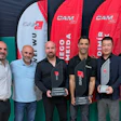 Six men posing at professional event with red CAM branded banners in background