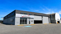 Klimat industrial warehouse facility with white metal exterior and service bay doors under clear blue sky