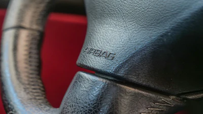 Airbag embossed text on gray leather car steering wheel with red interior visible