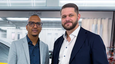 Two professional men in business attire posing in a modern office with large windows in the background