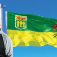Man in glasses smiling next to Saskatchewan provincial flag waving against blue sky