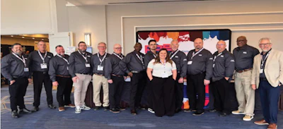 Group of professionals in dark jackets and lanyards posing together at an indoor event with colorful artwork backdrop