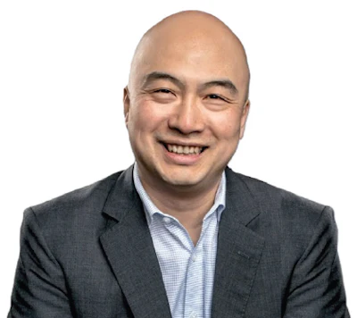 Professional headshot of an Asian man in business attire smiling at camera
