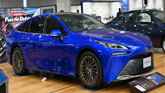 Blue Toyota Mirai hydrogen fuel cell vehicle displayed in showroom with gold-trimmed wheels