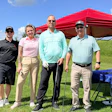 Four golfers pose together at an outdoor charity event under a red tent canopy
