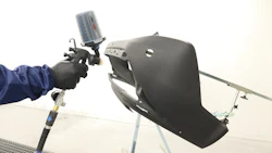 Worker spray painting black automotive part using HVLP spray gun in industrial facility