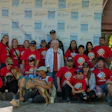 Large group of volunteers in matching red shirts posing together at outdoor community event with branded backdrop