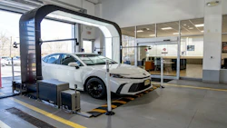 White Toyota sedan in automated car wash system at dealership showroom with glass offices visible