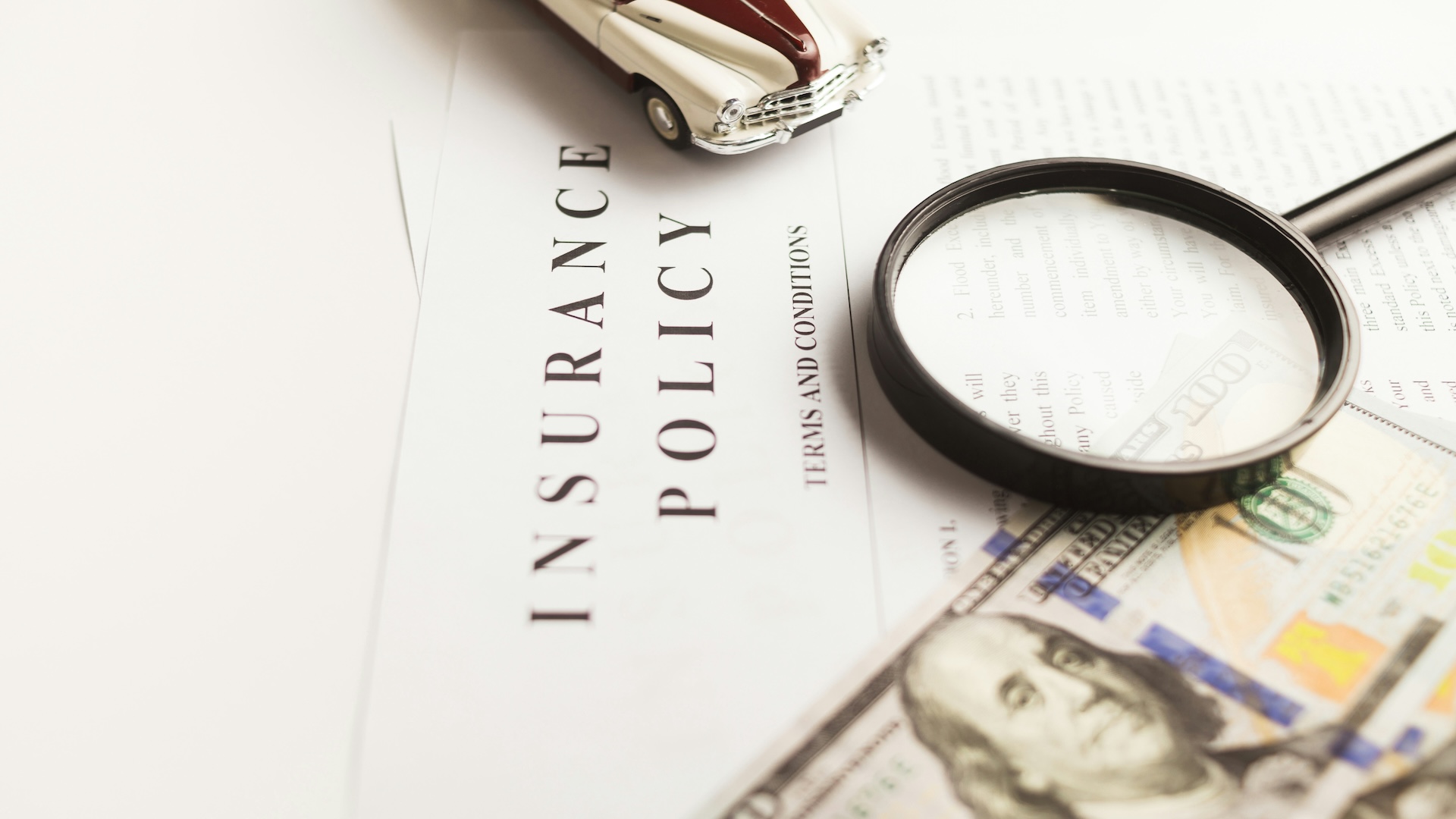 Insurance policy document with magnifying glass, dollar bills, and toy car for coverage concept