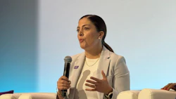 Professional woman speaking at conference panel with microphone, wearing beige blazer