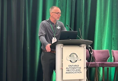 Man speaking at podium branded with Ontario Automotive Recyclers Association logo during presentation event