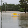 Flooded road with yellow water warning sign and submerged utility poles during severe flooding