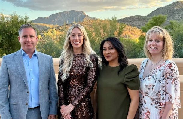 Four professionals posing together outdoors with desert mountains and cacti in the background
