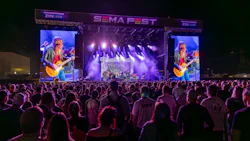Large outdoor concert stage with purple lighting, video screens, and crowd at SEMA FEST event