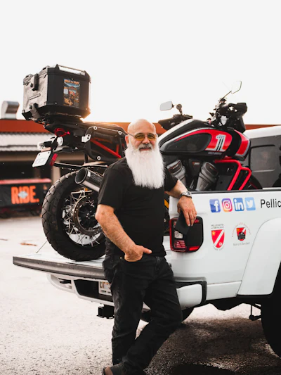 Bearded man in glasses posing with adventure motorcycle equipped with camera gear and travel luggage