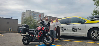 Group celebrates with red and black motorcycle next to white Mobile Hub branded van in urban parking lot