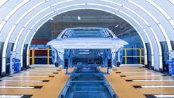 White car on assembly line in modern automotive manufacturing facility with industrial tunnel structure