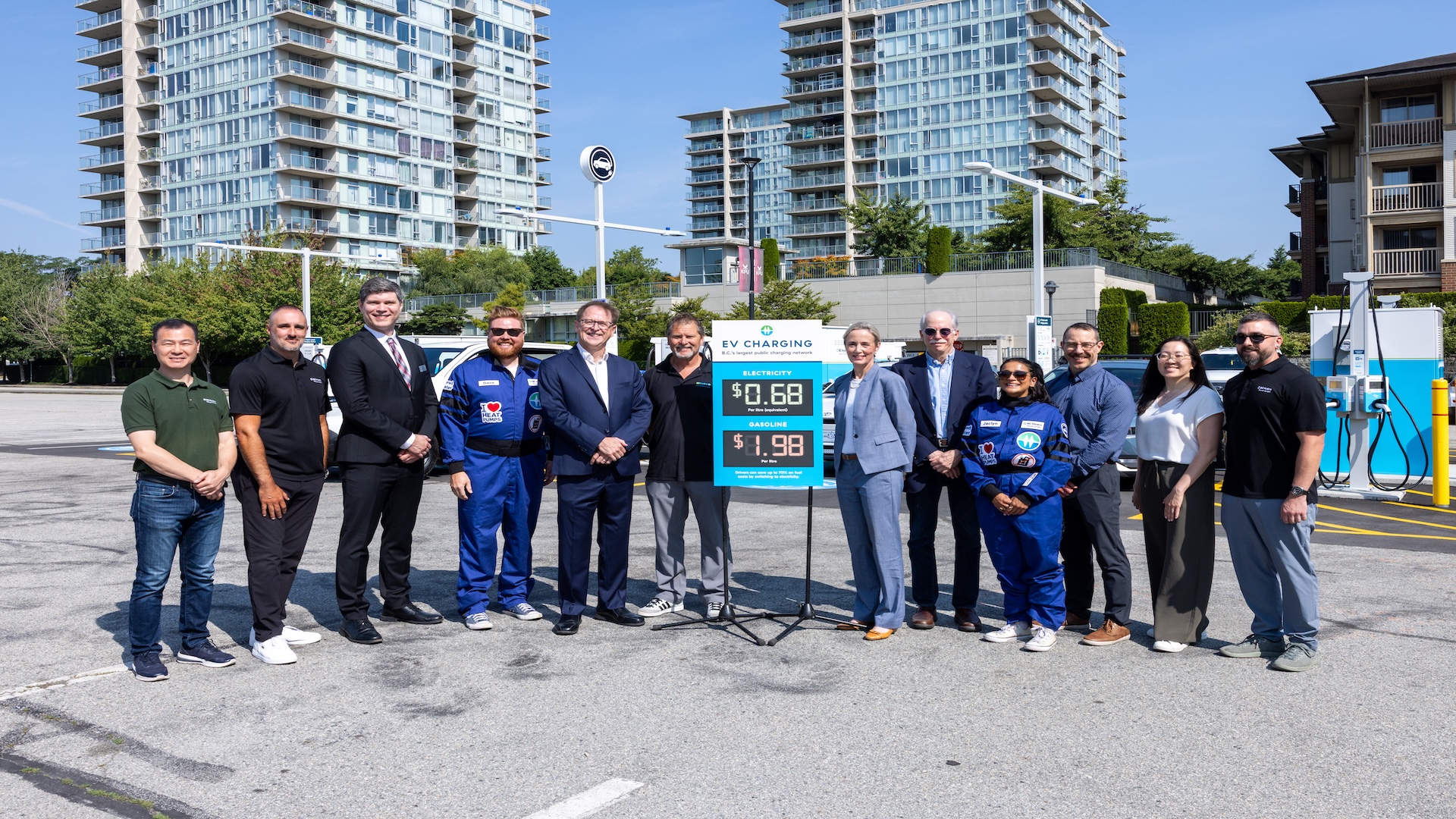 Group of officials and workers posing at gas station with price display and city buildings in background