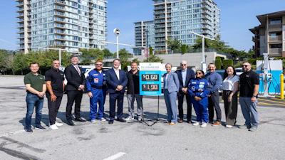 Group of officials and workers posing at gas station with price display and city buildings in background