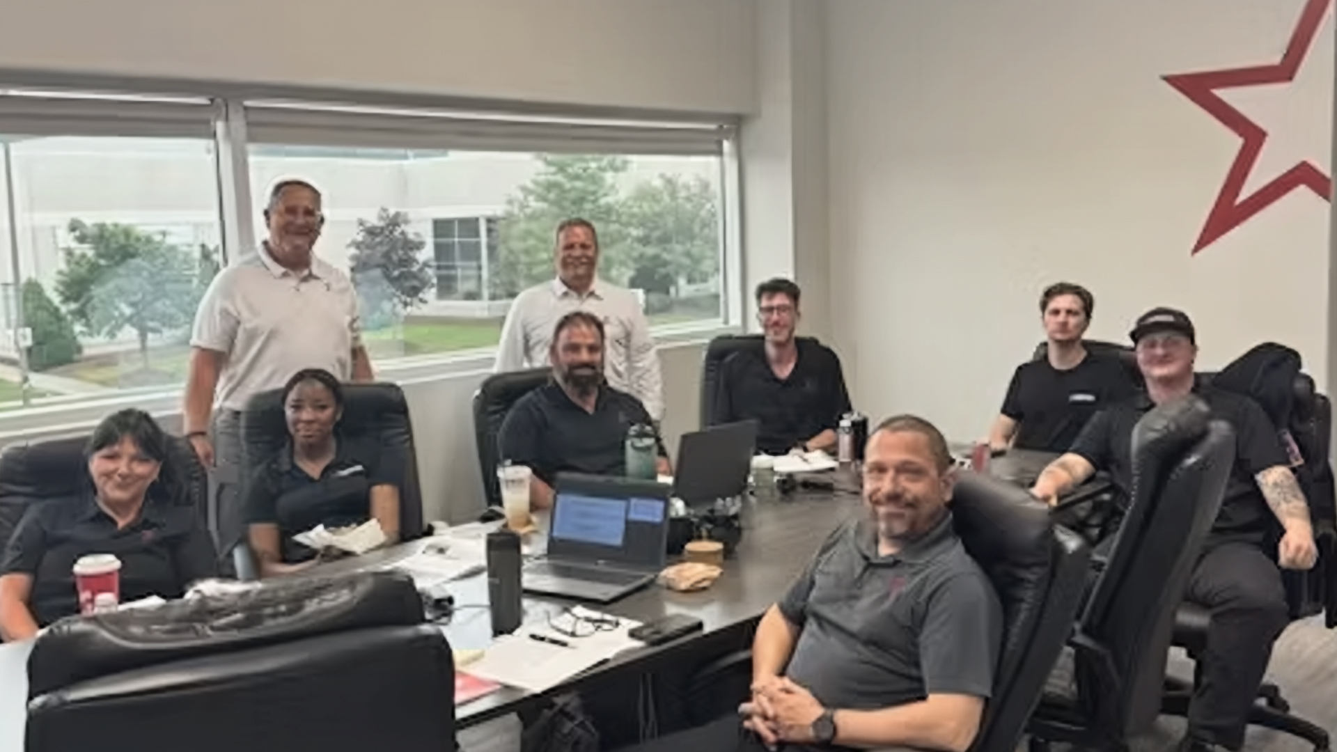 Team of 10 professionals gathered around a conference table in a bright office with windows overlooking green landscape