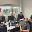 Team of 10 professionals gathered around a conference table in a bright office with windows overlooking green landscape