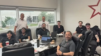 Team of 10 professionals gathered around a conference table in a bright office with windows overlooking green landscape