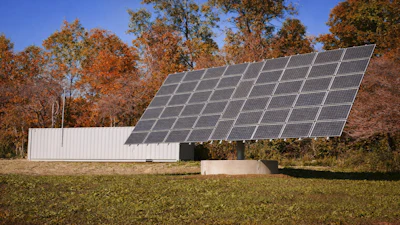 Large solar panel array mounted on white structure in autumn field with deciduous trees