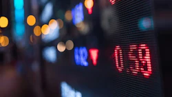 Nighttime urban street with blurred neon lights and red LED financial market display showing stock data