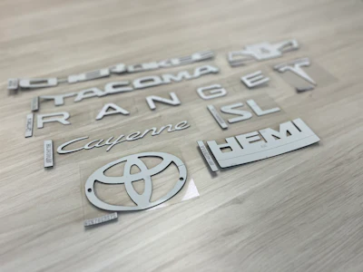 Chrome vehicle emblems and badges including Toyota logo arranged on wooden surface