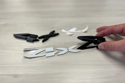 Hand cutting apart a black logo with scissors on wooden surface with scattered pieces
