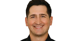 Professional headshot of smiling man in black button-up shirt against white background