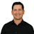 Professional headshot of smiling man in black button-up shirt against white background Headshot