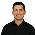 Professional headshot of smiling man in black button-up shirt against white background