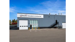 Modern industrial facility with gray exterior, white garage doors, and company signage under clear blue sky