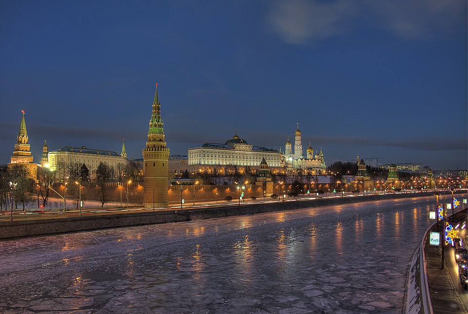Moscow Kremlin illuminated at dusk with golden-lit towers reflected in the frozen Moscow River