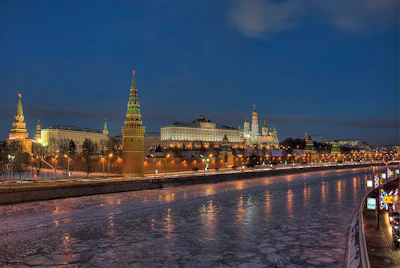 Moscow Kremlin illuminated at dusk with golden-lit towers reflected in the frozen Moscow River