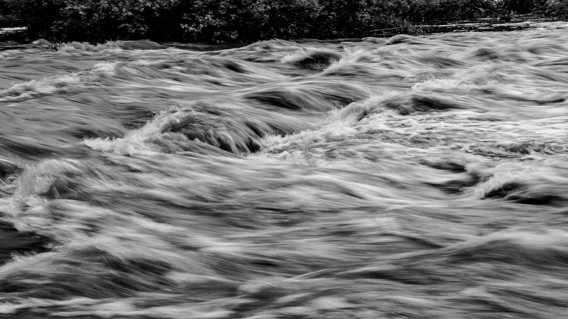 Flowing river rapids with motion blur and cascading white water against dark rocks