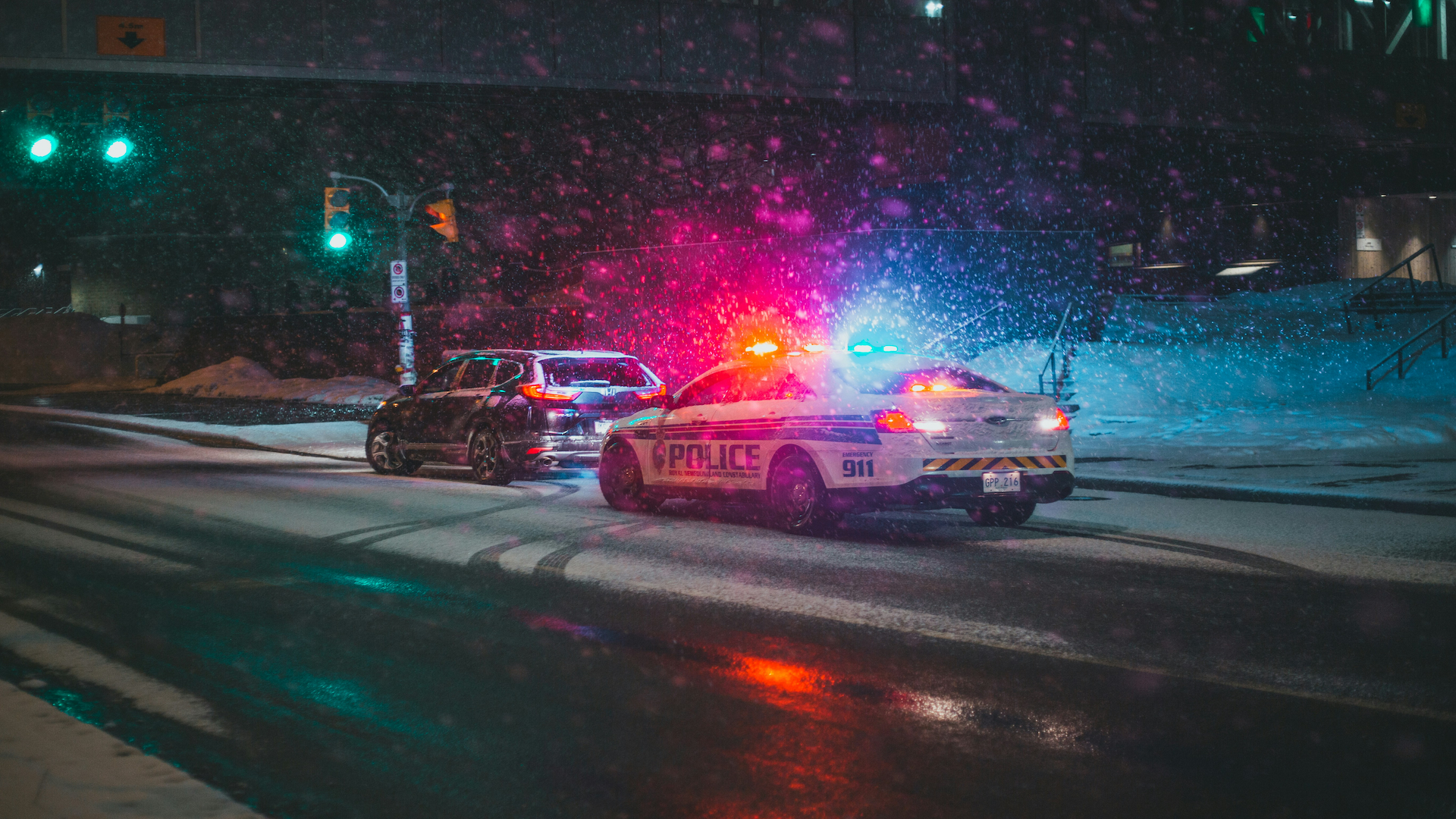 Police car with flashing red and blue lights responding at night on a wet street with colorful light effects