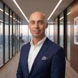 Professional man in navy blazer standing in modern high-rise office corridor with city skyline views