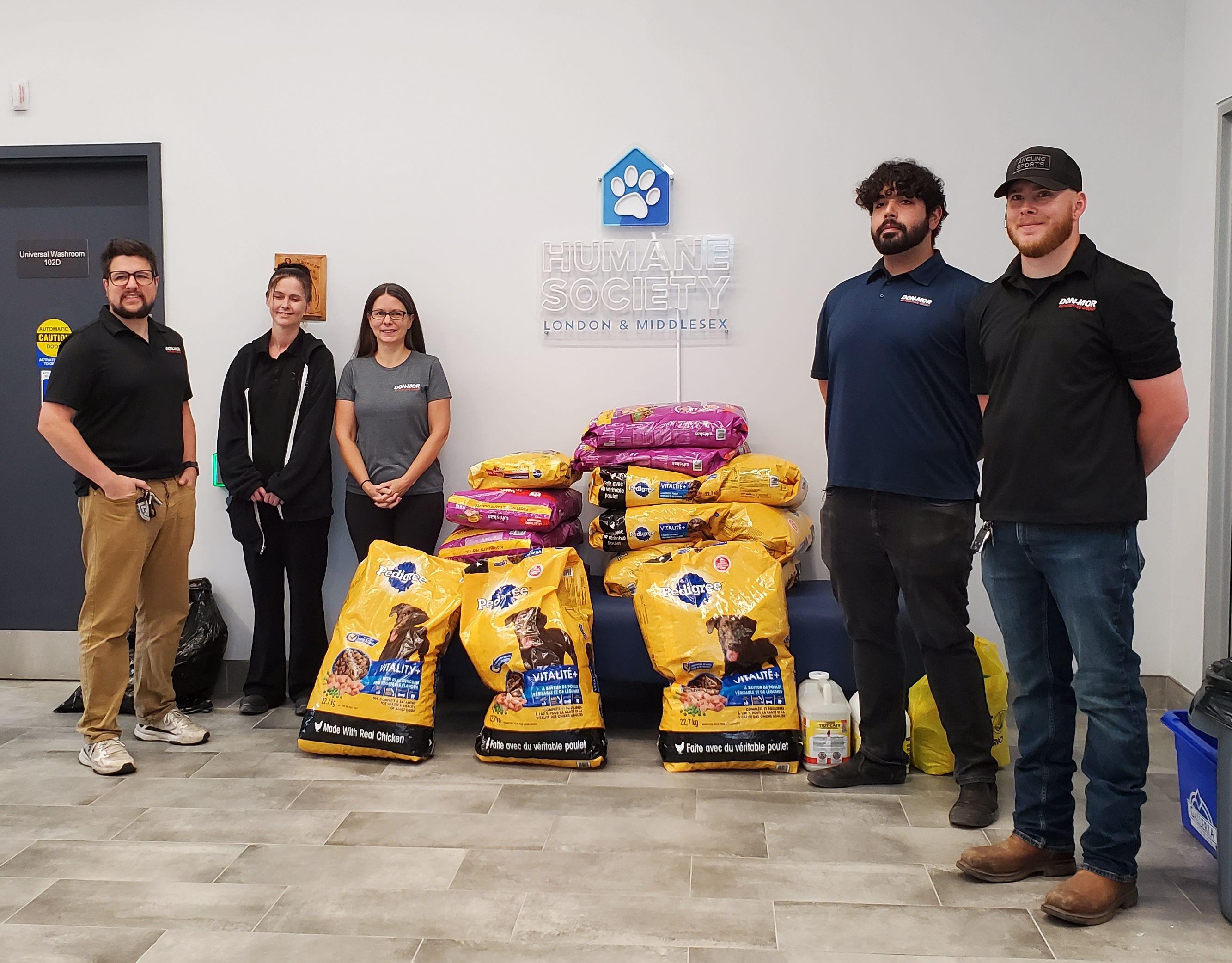 Five staff members stand with stacked bags of pet food donations in front of Humane Society London & Middlesex logo