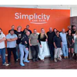 Simplicity Car Care team of employees posing together in front of orange branded wall signage