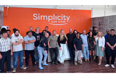 Simplicity Car Care team of employees posing together in front of orange branded wall signage