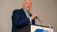 Professional man in navy blazer speaking at podium with microphone during corporate event
