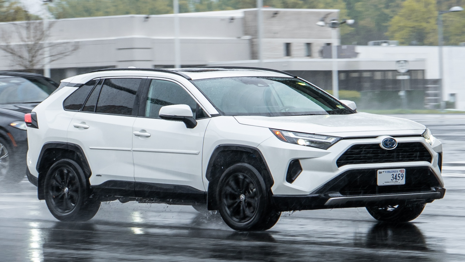 White Toyota RAV4 SUV with black wheels parked on wet pavement near industrial building