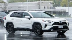 White Toyota RAV4 SUV with black wheels parked on wet pavement near industrial building
