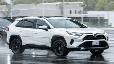 White Toyota RAV4 SUV with black wheels parked on wet pavement near industrial building