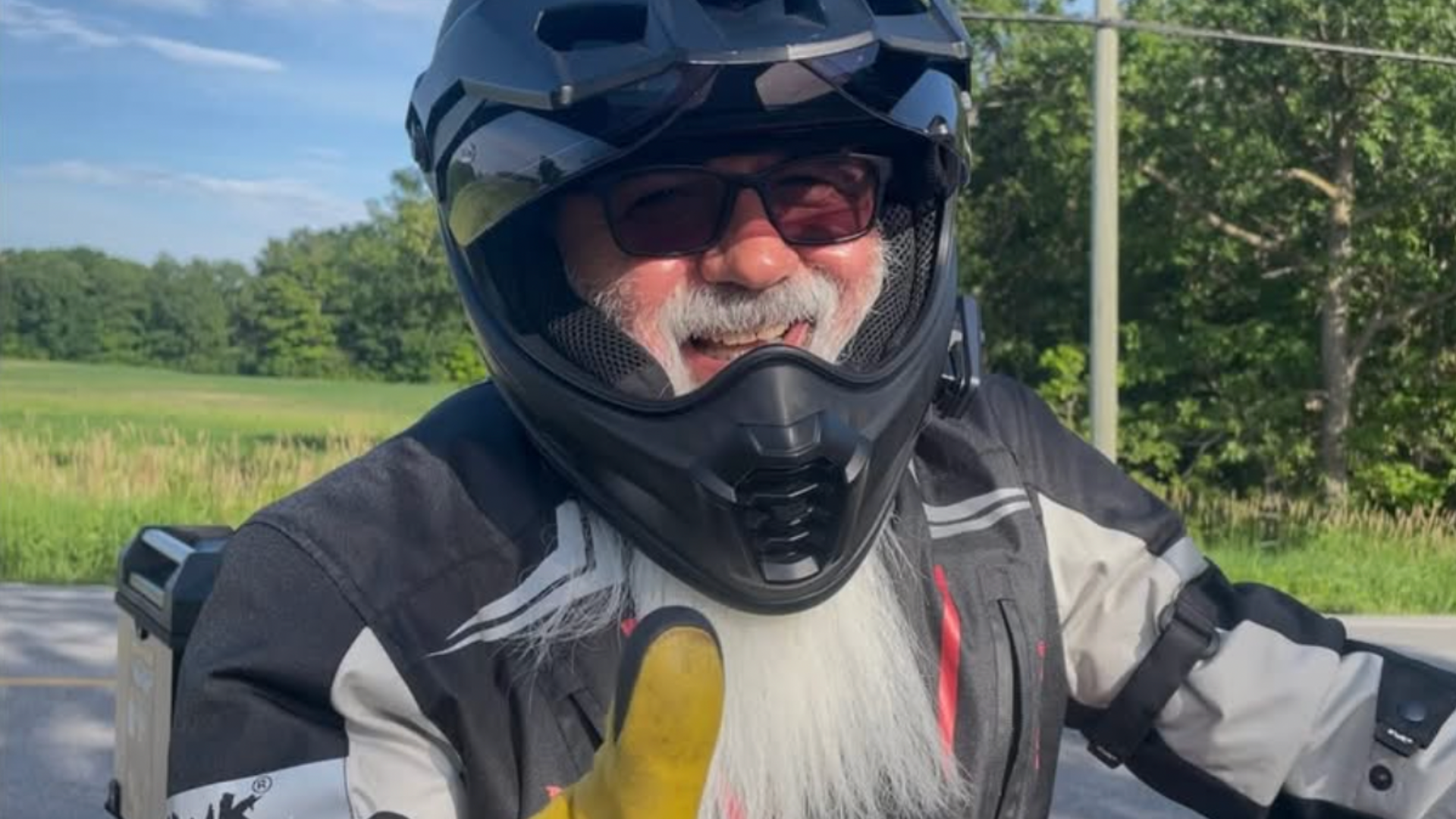 Person wearing black motorcycle helmet and protective gear outdoors with green field background