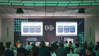 Iris Global Forum conference presentation with speaker addressing audience in modern venue with teal-lit ceiling and dual projection screens